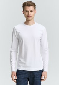 Langærmet hvid bomulds T-shirt med rund hals, glat tekstur og tætsiddende design, parret med mørkeblå jeans.