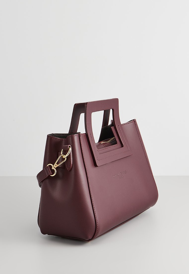 Sac à main en cuir bordeaux au design structuré, doté d'une ouverture rectangulaire, de quincaillerie dorée et d'une bandoulière amovible.