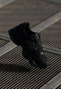 Baskets de sport noires en mesh et caoutchouc, de forme arrondie, avec des surfaces texturées et un logo bien visible sur le côté.
