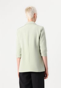 Světle zelený blazer se třičtvrtinovými rukávy a přizpůsobeným designem. Hladká textura, jediný zadní šev a žádné viditelné zapínání.