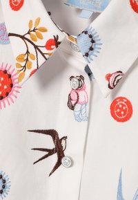 Valge särk värvikate tikanditega, sealhulgas lilled, linnud ja karu. Omab teravat kraed ja nuppe karumotiiviga.