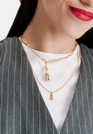Goldkette und Anhängerhalsketten, die an einer Person getragen werden. Eine Halskette zeigt einen strukturierten Anhänger, während die andere eine feine Kette mit einem kleinen Charm ist.