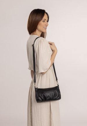 Schwarze Lederhandtasche mit einer weichen, gerafften Textur, verstellbarem Tragegurt und einem einfachen Reißverschlussverschluss. Im Crossbody-Stil getragen.
