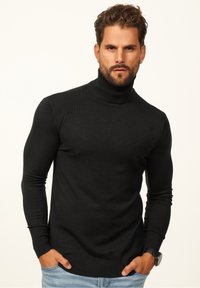 Black turtleneck sweater made of a soft material, fitted design with ribbed cuffs and hem, worn with light blue jeans.