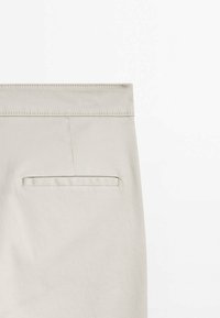 Pantalon beige avec une ceinture plate, une poche arrière unique, et une texture de tissu en coton lisse. Conception simple, sans motifs visibles ni détails matériels.