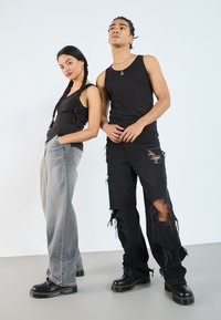 Svart tank top, grå vide ben jeans med løs passform, og svart slitt bukser. Begge har på seg svarte støvler med tykk såle.