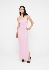 Εφαρμοστό ροζ φόρεμα bodycon με τετράγωνη λαιμόκοψη, λεπτές τιράντες και πλαϊνό σκίσιμο, συνδυασμένο με μαύρες σανδάλια με λουράκια. Λείο υλικό.