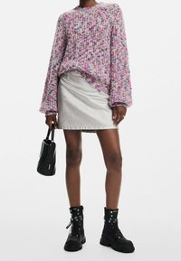 Pull coloré en tricot à manches longues, associé à une jupe en denim argenté. Bottes de combat noires et petit sac noir clouté.