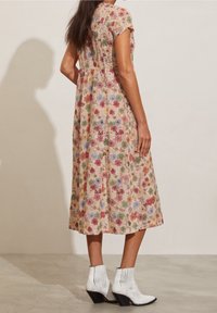 Robe midi à motif floral sur un fond clair avec des fleurs multicolores. Présente des manches courtes, un corsage ajusté et une jupe fluide. Associée à des bottines blanches.