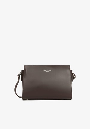 Sac bandoulière en cuir marron Lancaster Paris avec logo argenté sur le devant et sangle ajustable sur fond blanc.
