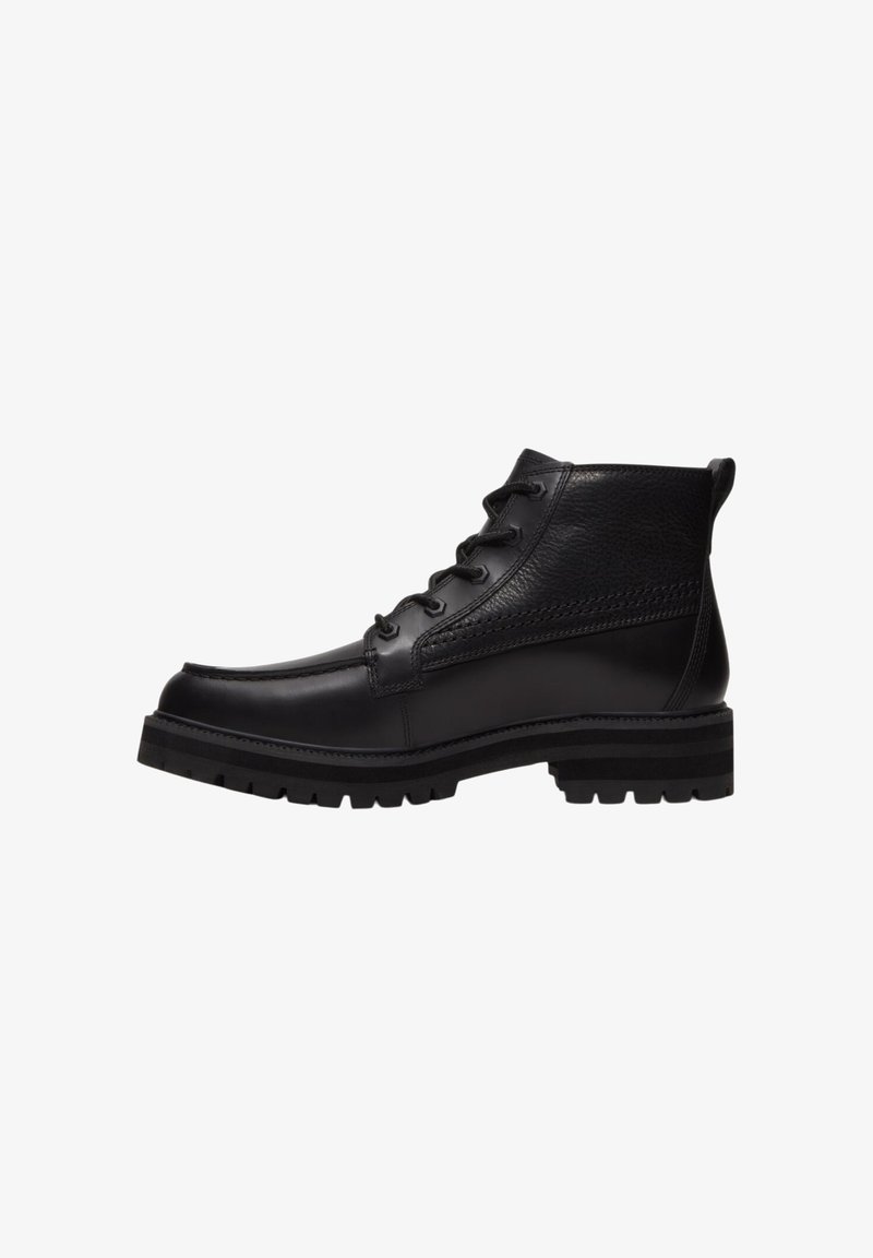 Bottine noire en cuir avec fermeture à lacets à l’avant, col texturé, semelle épaisse à crampons et languette au talon, présentée de profil sur fond blanc.