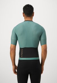 Kortärmad cykeltröja i teal med texturerad tyg, med svart midjestöd och guldlogotyp. Kroppsnära design.