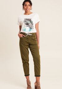 T-shirt blanc avec un graphique de feuille de palmier noir et turquoise ; associé à un pantalon de jogging tapered vert olive avec taille à cordon et poches avant.