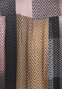 Mehrfarbiger Stoff mit Zickzackmustern in Rosa-, Schwarz- und Goldtönen. Die Textur wirkt glatt mit leichtem Schimmer.