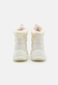 White faux fur-lined ankle boots with quilted detailing, padded design, and a rubber sole featuring the brand name embossed on the back.