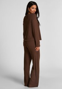 Bruin geribd loungewear set met een losvallende top met lange mouwen en bijpassende wijde broek, die een gestructureerd gebreid ontwerp laat zien.