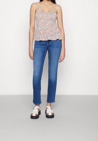 Top peplum floreale con spalline sottili, dotato di vita arricciata. Indossato con jeans blu a gamba dritta e sandali con piattaforma bianchi.