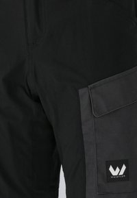 Svarta shorts med en slät yta, med en sidoficka och en kontrasterande mörkgrå panel. Inkluderar en logotypmed patch med vita grafiska detaljer.