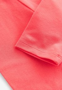 Koraal katoenstof met licht gestructureerd oppervlak; close-up van een mouwzoom met een nette stiksel.