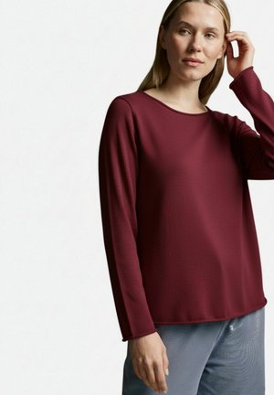 Burgundy long-sleeve top with a round neckline and textured fabric, paired with light blue, shiny pants. Loose fit and casual design.