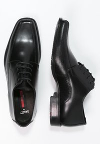 Chaussures habillées en cuir noir présentant une texture lisse et perforée, des lacets et un petit talon carré. Forme classique avec des bouts carrés.
