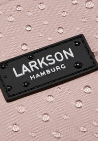 Tessuto rosa con superficie testurizzata e gocce in rilievo. Un'etichetta nera con testo bianco che recita "LARKSON HAMBURG" è mostrata in modo prominente.