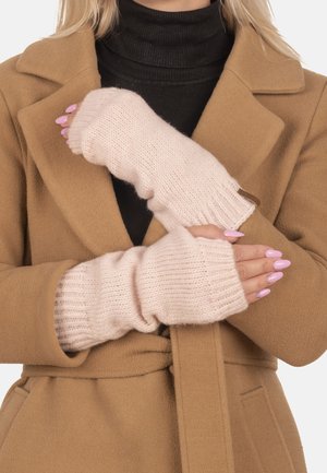 Helle rosa gestrickte fingerlose Handschuhe mit geripptem Muster, getragen über einem schwarzen Rollkragenpullover, kombiniert mit einem beigen Mantel.