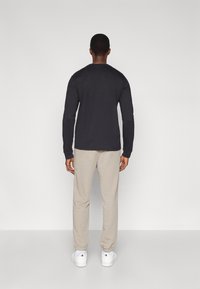 Μαύρο πουκάμισο με μακριά μανίκια, μπεζ φόρμα και λευκά αθλητικά παπούτσια. Ομαλό ύφασμα, άνετη εφαρμογή με ριμπ μανσέτες, εμφανίζεται από πίσω.