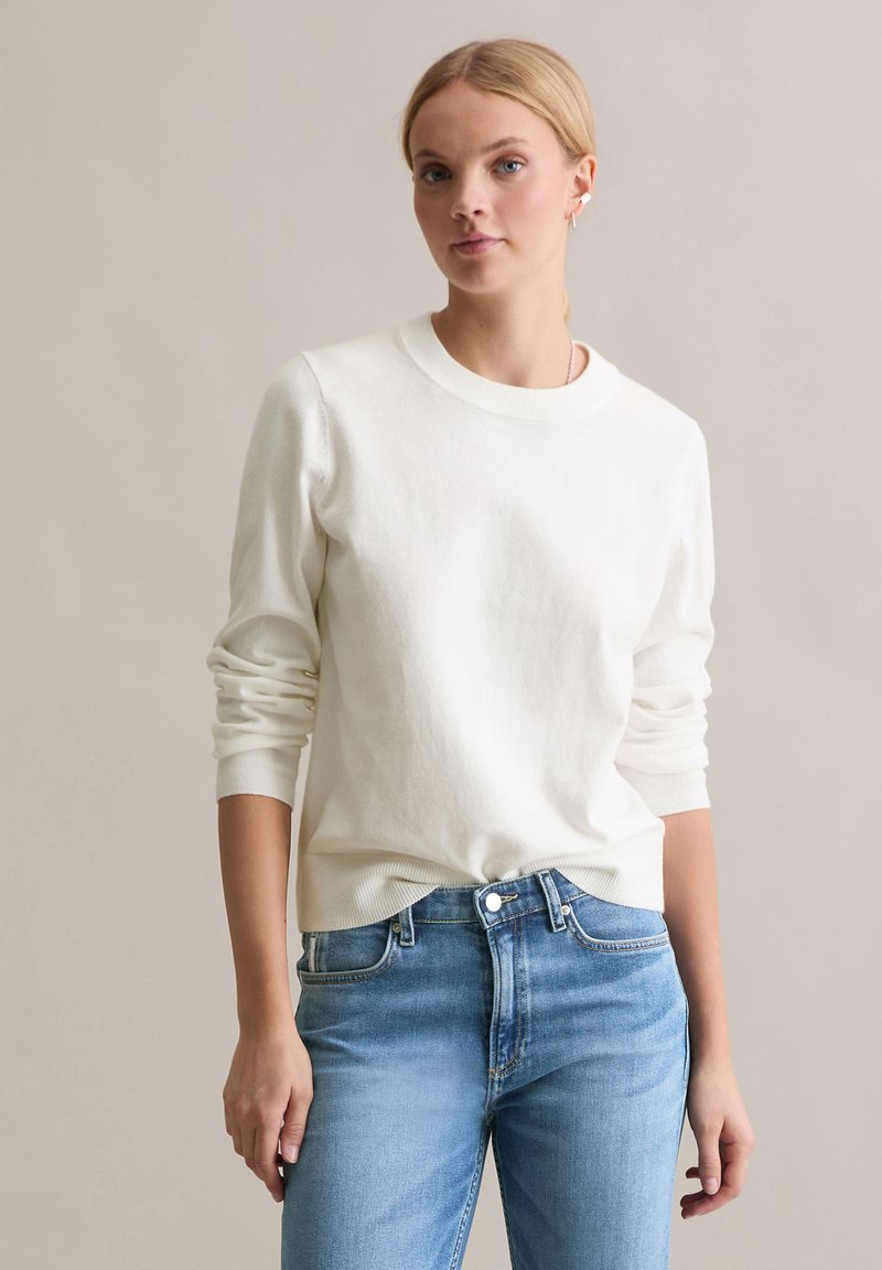 Witte crewneck trui met geribbelde manchetten en zoom, gecombineerd met lichtblauwe denim jeans, met een getailleerd ontwerp en een medium gewassen textuur.