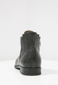 Musta nahkasaapas nilkkapituudella, jossa on sileä pinta, sivussa vetoketju ja matala pinottu korko tuen tarjoamiseksi.