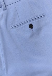Hellblaue Hosen aus glattem Stoff mit einer Gesäßtasche, die einen einzelnen schwarzen Knopf und Bügelfalten aufweist.
