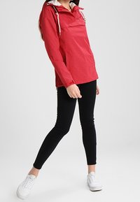 Rød, mønstret pullover-jakke med hætte, hvid foring og snore. Sat sammen med sorte leggings og hvide sneakers.