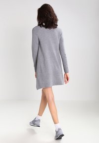 Abito a maglia grigio con maniche lunghe e una vestibilità ampia, che arriva a metà coscia, abbinato a scarpe da ginnastica grigie e calzini bianchi.