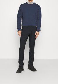 Felpa navy con collo rotondo, abbinata a pantaloni neri slim-fit. Scarpe da ginnastica nere completano l'outfit. Tessuto semplice, dalla texture morbida.