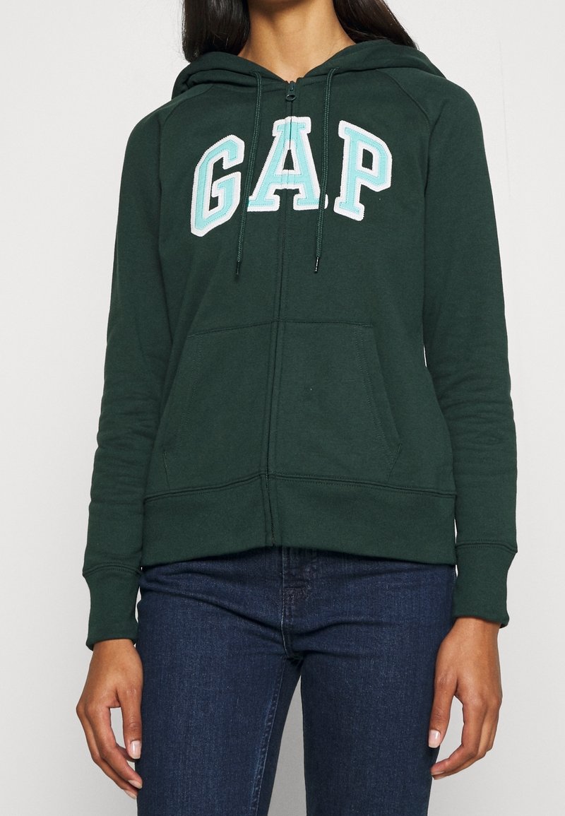 Felpa verde con zip realizzata in tessuto morbido, caratterizzata da un grande logo "GAP" bianco e azzurro chiaro sul davanti, con tasca a marsupio e cappuccio con cordino.