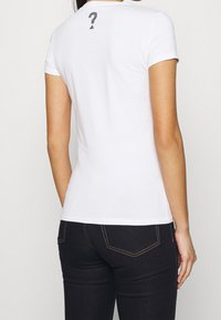 Camiseta de algodón blanca de manga corta, con un diseño de signo de interrogación negro en la parte posterior cerca del cuello. Forma simple y ajustada.