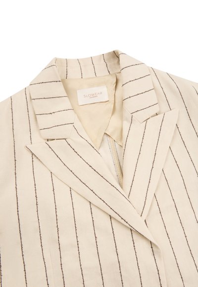 Beiger Blazer mit dünnen vertikalen schwarzen Streifen, breiten Revers und beigefarbenem Innenfutter, mit einem Slowear-Brandetikett am Kragen innen.