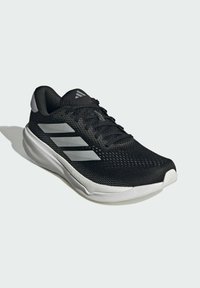 Black athletic sneaker with a mesh upper, silver three-stripe design, textured outsole, and contrasting white sole. Minimalistic design.