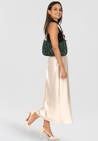 Bolso acolchado verde con detalles en metal dorado, combinado con una blusa negra y una falda de satén crema. Zapatos de tacón nude.