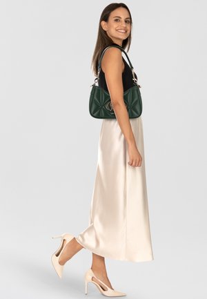 Sac à main matelassé vert avec des détails en métal doré, associé à un haut noir et une jupe en satin crème. Chaussures à talons nu.