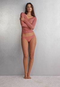 Langarm-Blush-Oberteil mit Spitzenbesatz, kombiniert mit passender nahtloser Unterwäsche. Glattes Material mit figurbetontem Design, vor einem neutralen Hintergrund präsentiert.