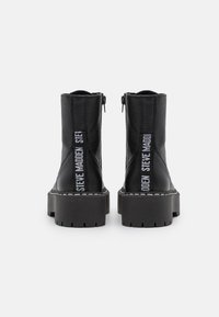 Bottines en cuir noir avec des semelles épaisses et texturées. Elles présentent une fermeture éclair sur le côté et des détails de marque en blanc le long de l'arrière.