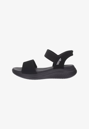 Sandalo nero slip-on con suola imbottita, cinturino elastico alla caviglia e punta aperta, con il marchio "Skechers Slip-Ins" sulla fascetta laterale.