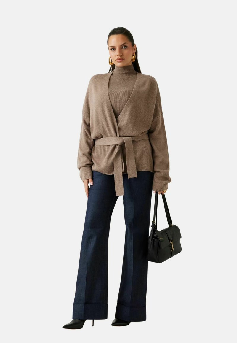 Cardigan marrone a maglia con cintura, indossato sopra un dolcevita coordinato; abbinato a pantaloni larghi scuri e borsa nera. Scarpe con tacco nere.