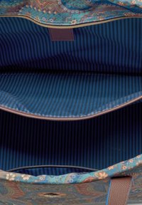 Innenraum einer mehrfarbigen Stofftasche mit floralen Mustern, blauen und braunen gestreiften Futter und einer Reißverschlusstasche. Glatte Textur mit stabiler Form.