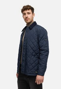 Marineblaue gesteppte Jacke mit einem Cordkragen, Druckknöpfen und Seitentaschen, aus einem glatten synthetischen Material gefertigt.