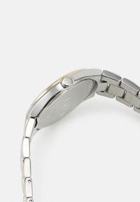 Reloj de acero inoxidable plateado con una caja redondeada, bisel suave y una pulsera de eslabones. Presenta un diseño minimalista y un detalle del logotipo en la corona.