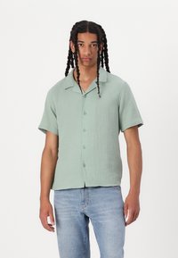 Korte mouwen, overhemd met kraag in een gestructureerde lichtgroene stof met knopen, gecombineerd met blauwe denim jeans. Casual pasvorm en eenvoudig ontwerp.