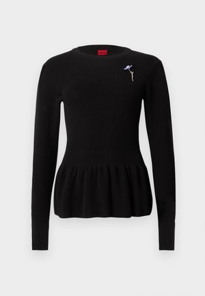 Pull noir en maille avec un ourlet à volant, manches longues et encolure ronde. Comprend un petit détail de broche florale bleue.