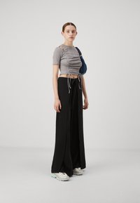 Grey ribbed cropped top with side cutouts and drawstring detail, paired with black wide-leg pants. White sneakers with pastel accents.